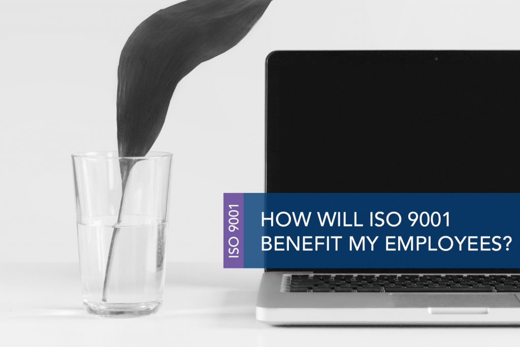 Black and white image of a turned off laptop screen and a glass of water next to it with a large plant leaf shooting out from the glass