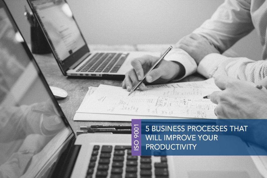 Black and white image of two people at a table with a pen and computer each. They are looking at a written on piece of paper