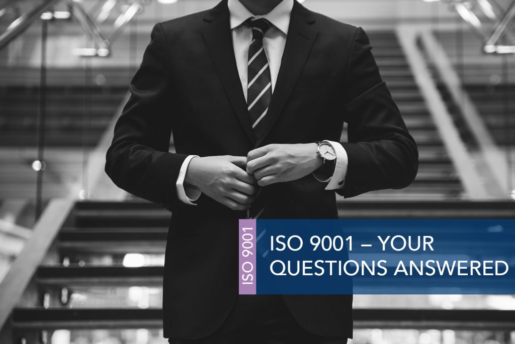 Black and white image of a person in a dark suit and tie, pulling the blazer across themselves